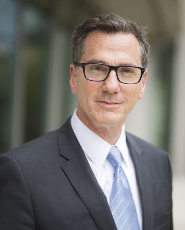 A portrait of Lee Feinstein ’81. Feinstein has dark hair and a dark suit with a blue tie.