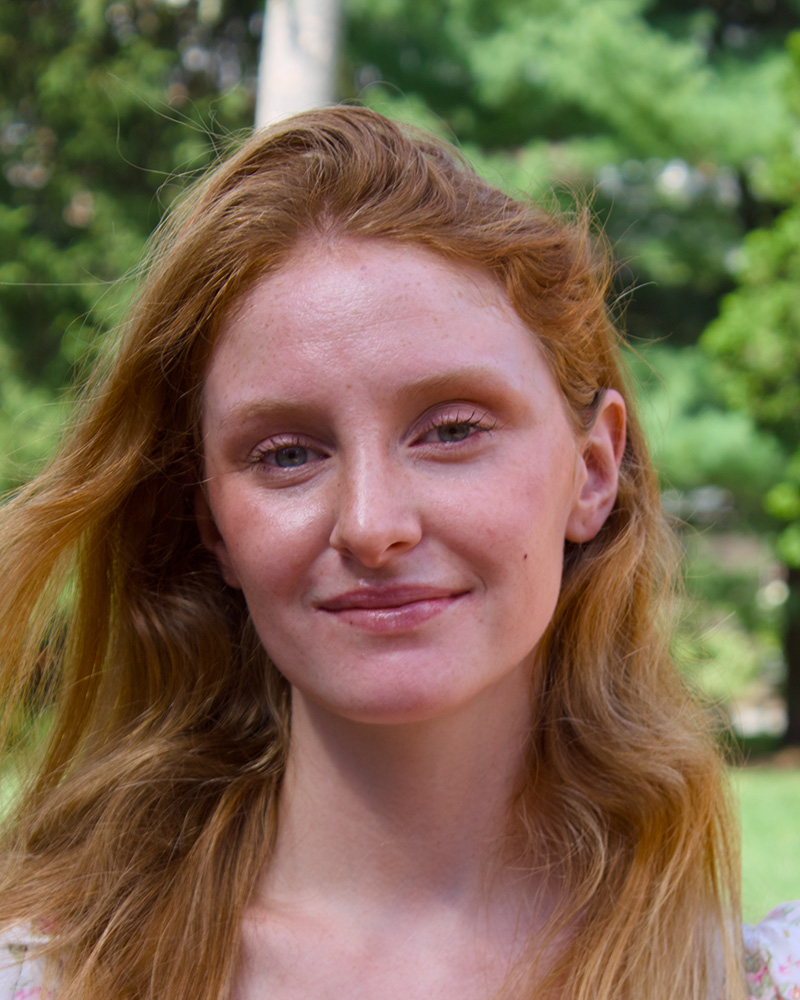 Smiling portrait of a student outdoors with trees in the background.