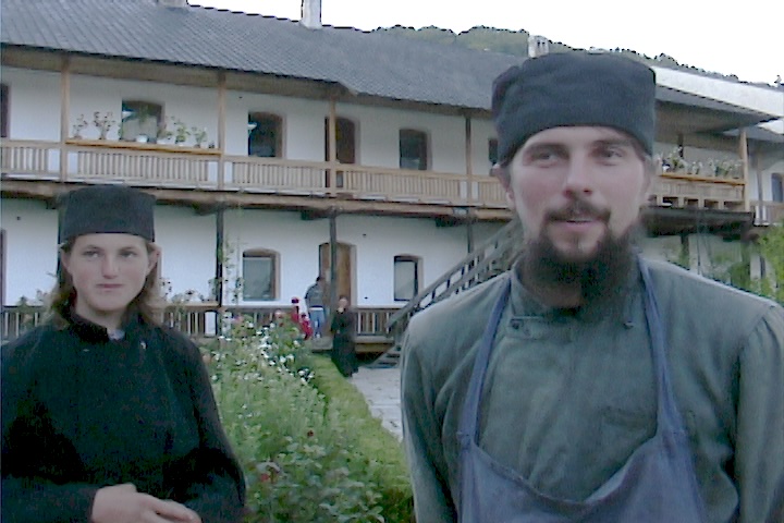 Two monks outside a building talking to a camera.