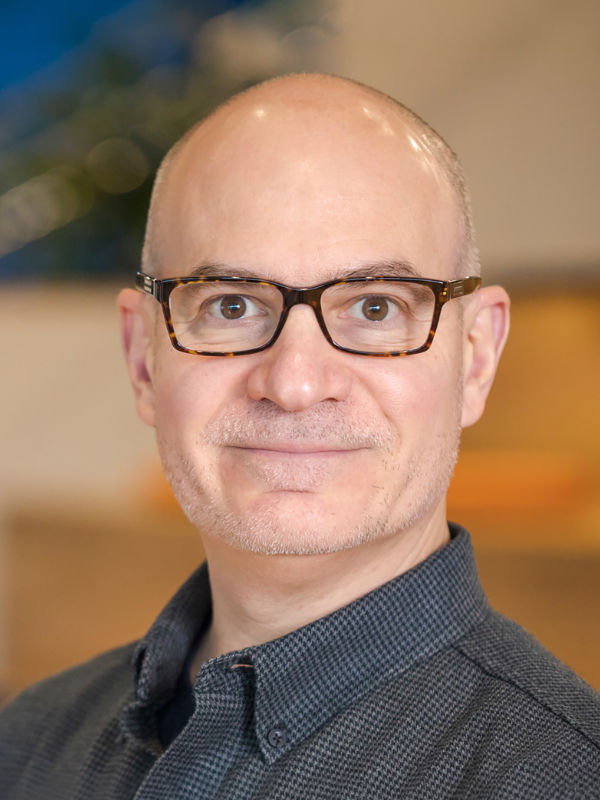 A photo of Michael Neuwirth ’89, a person with no hair, glasses, and a dark gray shirt.