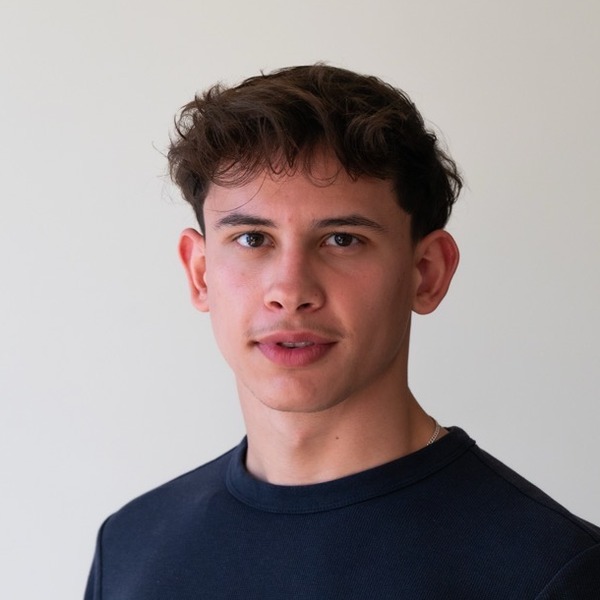 A portrait of Andi Buqa, a person with brown hair, wearing a navy crew-neck shirt.