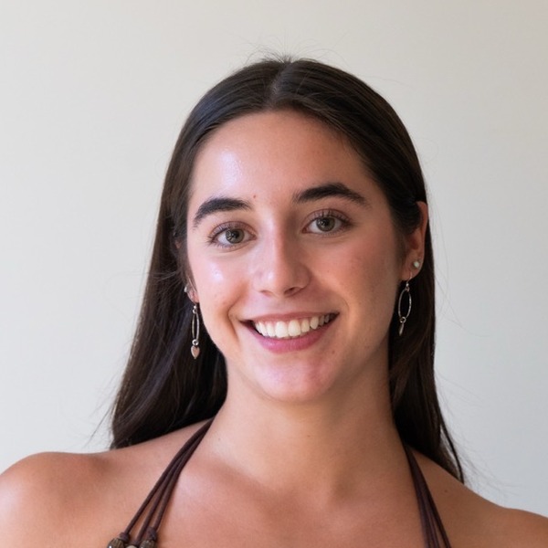 A portrait of Alessia Riera, a person with dark brown hair, wearing a striped halter top and hoop earrings.