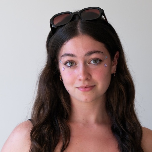 A portrait of Amalia Mesa, a person with brown hair, wearing sunglasses on their head and a black sleeveless top.