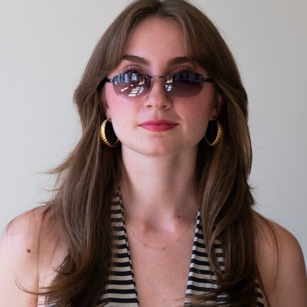 A portrait of Anjali Turchiano, a person with brown hair, wearing tinted sunglasses, hoop earrings, and a striped halter top.