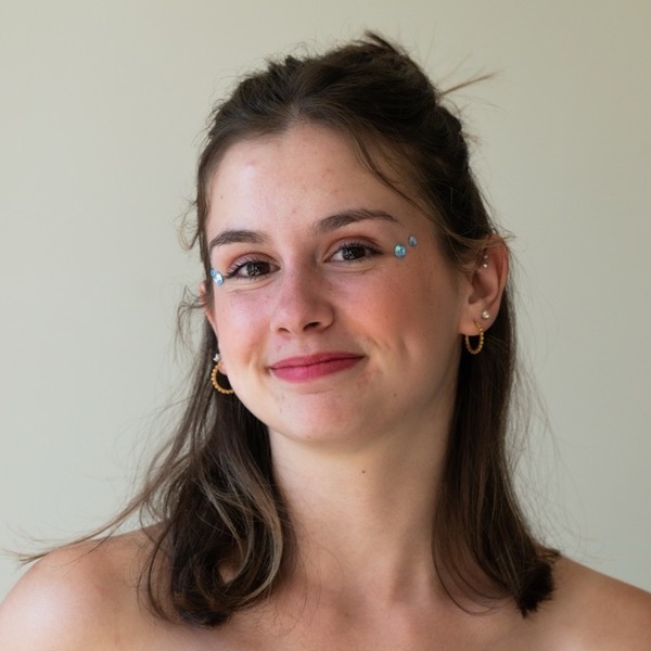 A portrait of Annabelle Fields, a person with brown hair, wearing a bright blue strapless top and hoop earrings.