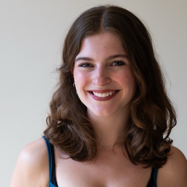 A portrait of Cara McGovern, a person with brown wavy hair, wearing a teal camisole.