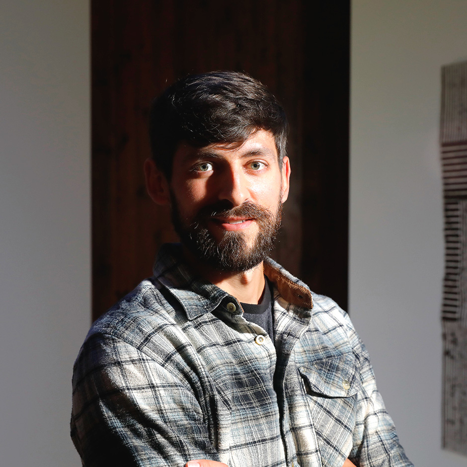 Person in a plaid shirt standing with arms crossed between two geometric artworks.