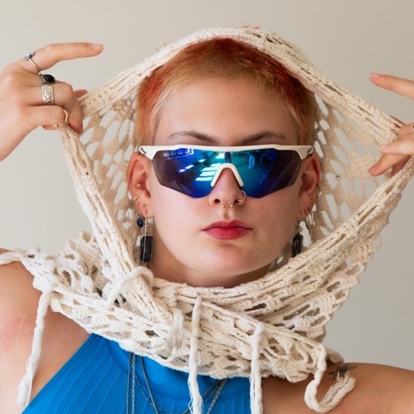A portrait of Lilli Palmer, a person with light red hair, wearing mirrored sunglasses, a bright blue sleeveless top, and a cream netted scarf.