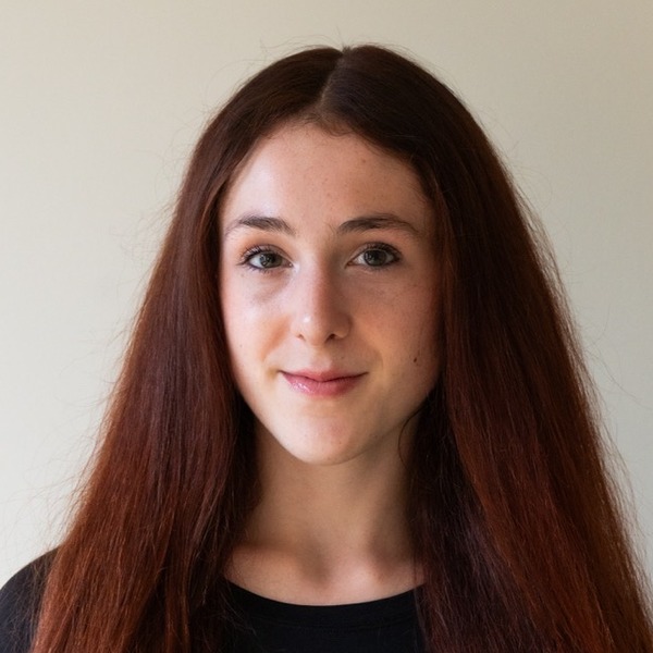 A portrait of Mia Salopek, a person with long red hair, wearing a black long-sleeved top.