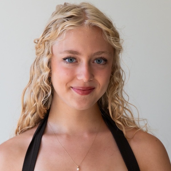 A portrait of Petra Brackett, a person with blonde curly hair, wearing a black halter top and pendant necklace.