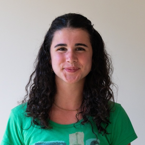 A portrait of Summer McTigue, a person with dark brown curly hair, wearing a green graphic T-shirt.
