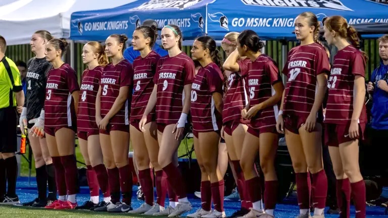 Soccer team standing on the sidelines looking on.