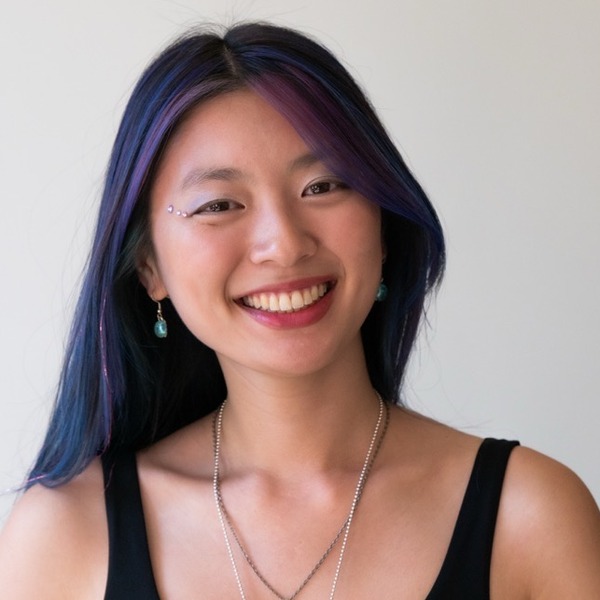A portrait of Zoë LaCheen-Fine, a person with long black hair and purple highlights, wearing a black sleeveless top and layered necklaces.