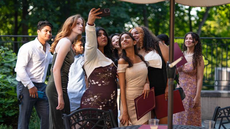 A large group of people huddled together outside with one person holding up their phone for a group selfie.