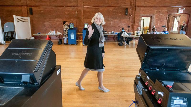 A person walking and waving to the camera at a polling site.