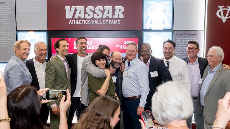 A celebratory group picture with a wall honoring the Hall of Fame inductees in the background.