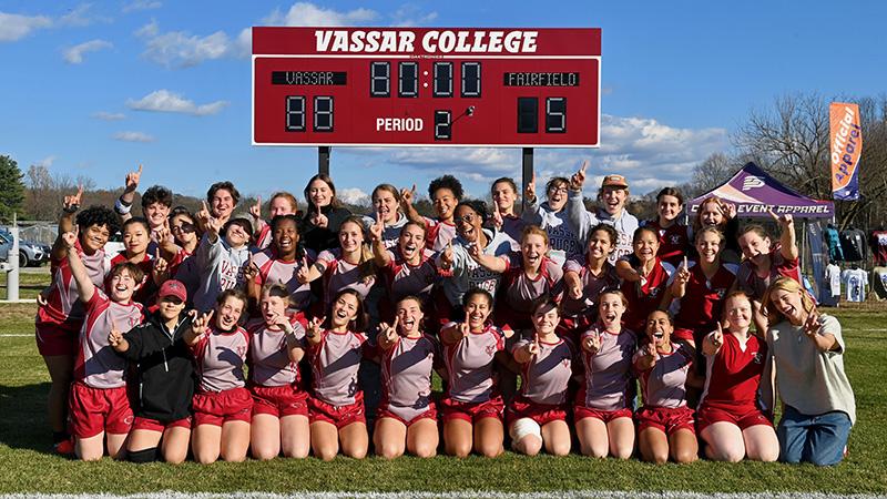 Elated team poses for group photo with the scoreboard in the background (Vassar 88, Fairfiled 5).