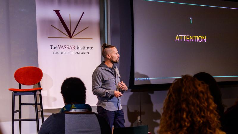 Person standing in front of a seated audience while addressing them.