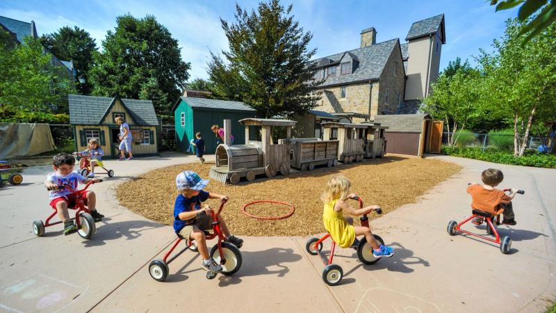 Children riding tricycles on a sidewalk.