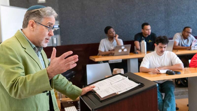 Person behind a lectern speaking into a microphone to a class.