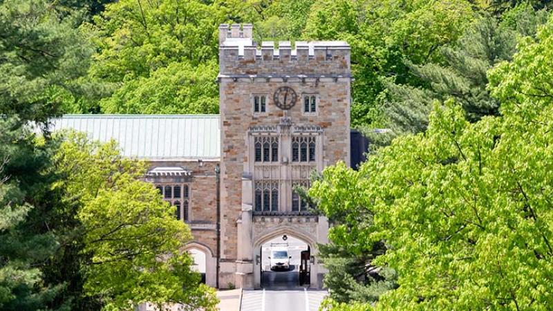 An aerial view of a gothic-style tower gate connected to buildings on either side, with lots of green trees in front and behind it.