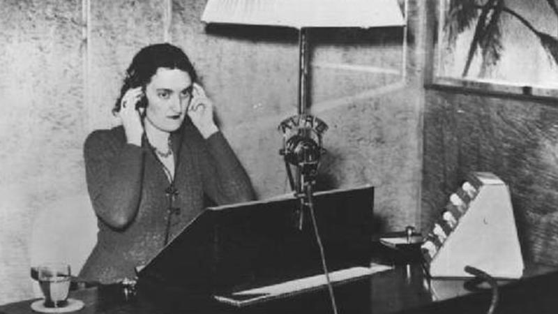 A person sitting at a desk listening intently with her hands pressed to the headphones that cover her ears.