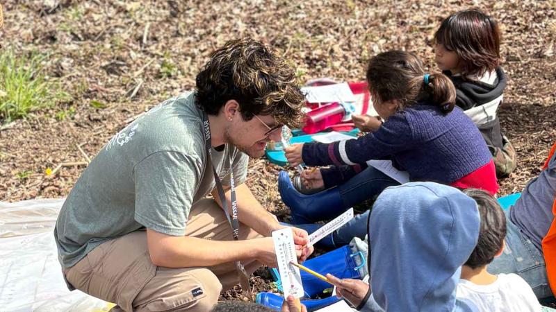 School age children with teacher in the field looking at thermometers.