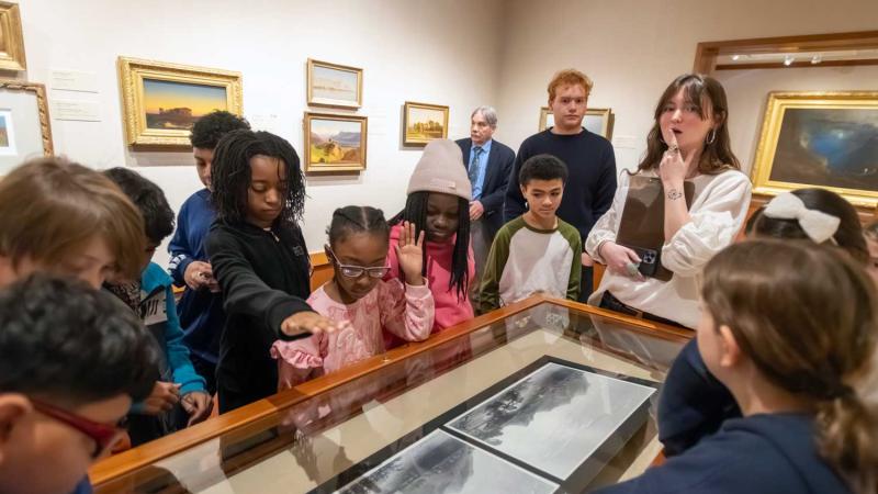 Students gathered around a glass case in a museum looking in.