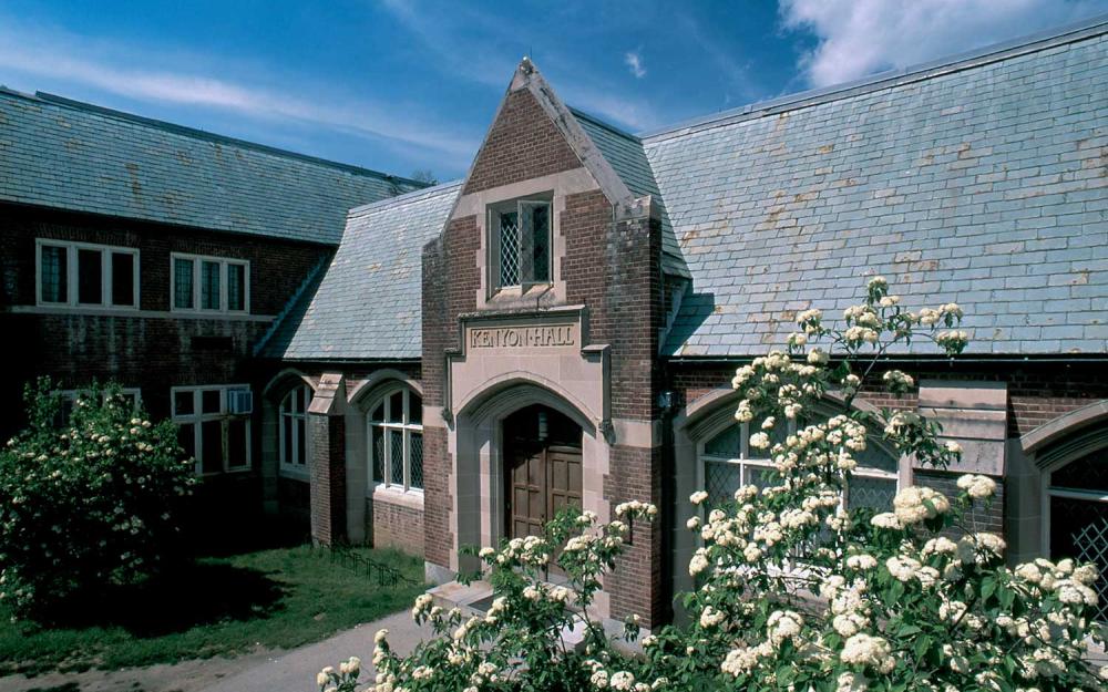 An outside photograph of Kenyon Hall, a brick building surrounded by bushes and flowers