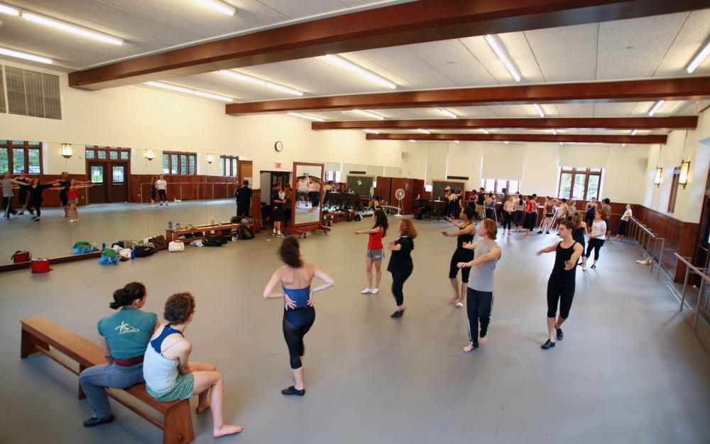 A large, well-lit dance studio in which dancers are practicing.