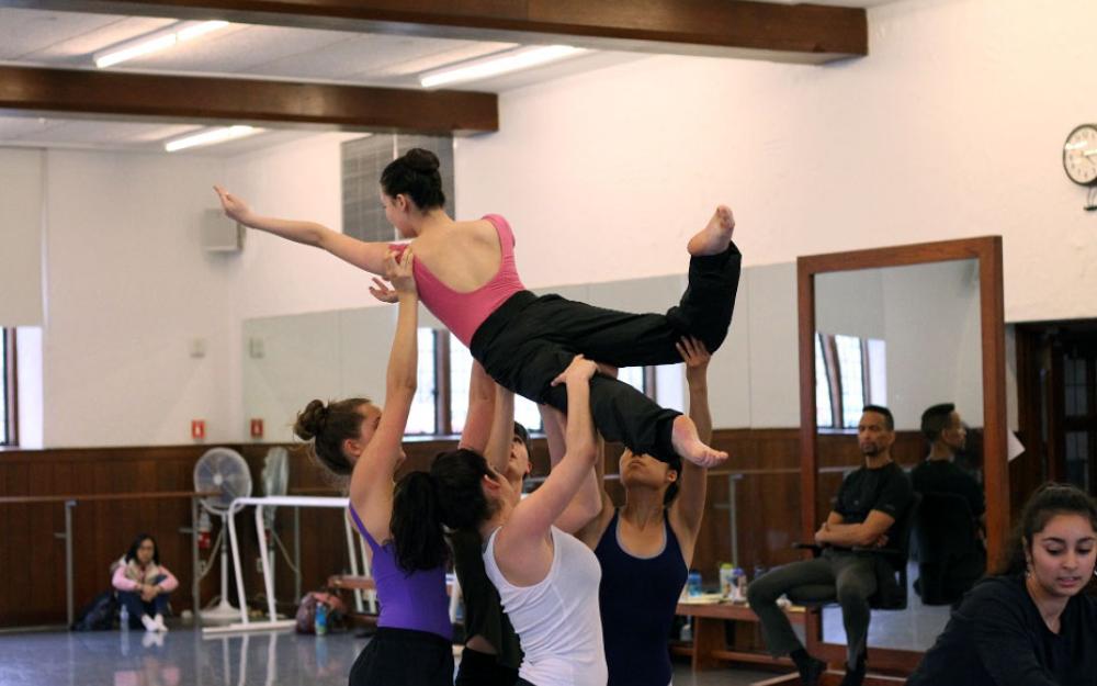 Four dancers hold a fifth dancer aloft in a studio.
