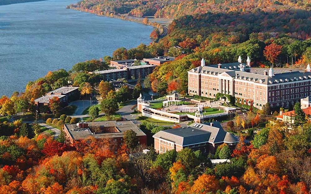 Aerial view of the Culinary Institute of America - large rectangle brick building surrounded by smaller buildings in a U shape next to the Hudson River with Fall foilage