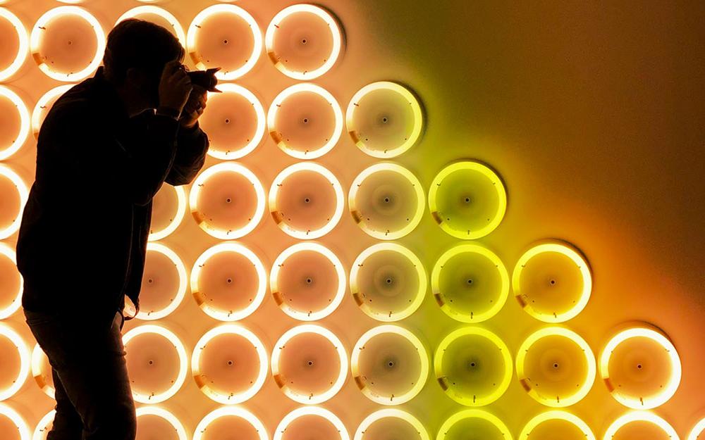 Circular neon lights forming a triangle with a photographer in shadow in front of it