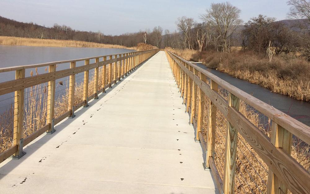 Cement and wooden bridge walkway over small lake a part of the Harlem Valley Rail Trail