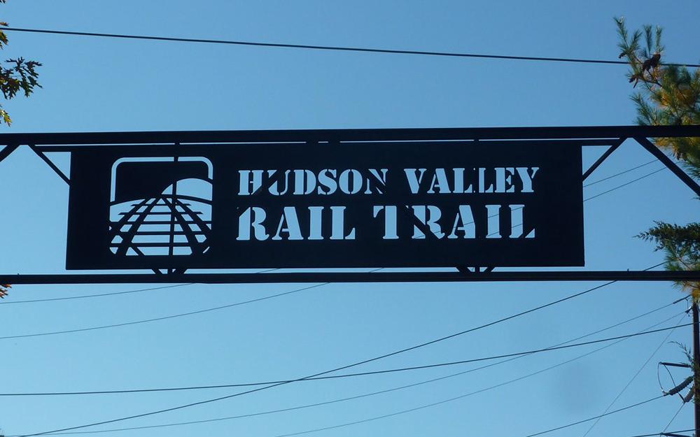 Black sign saying "Hudson Valley Rail Trial" hanging over the trail