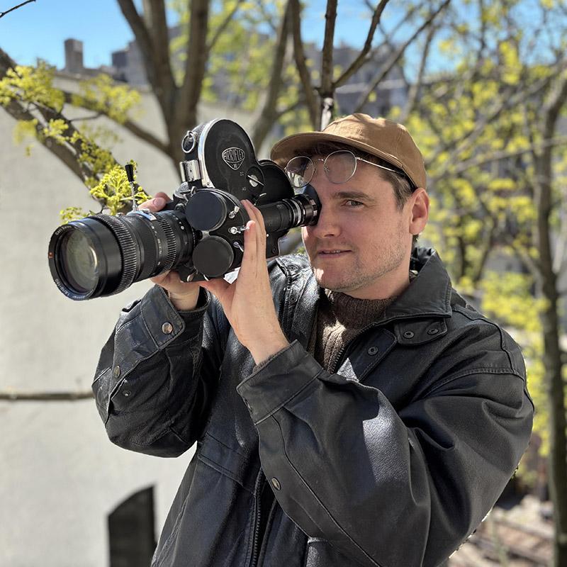 Pictured: Carl Elsaesser. Person holding an old fashion camera to their eye while standing outside.