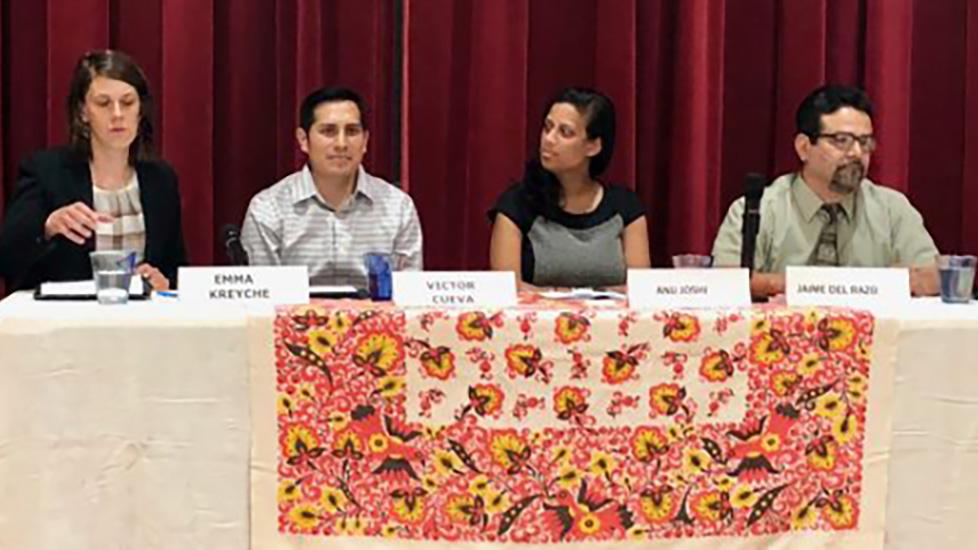 Four people sitting at the same side of a table with a curtain in the background.