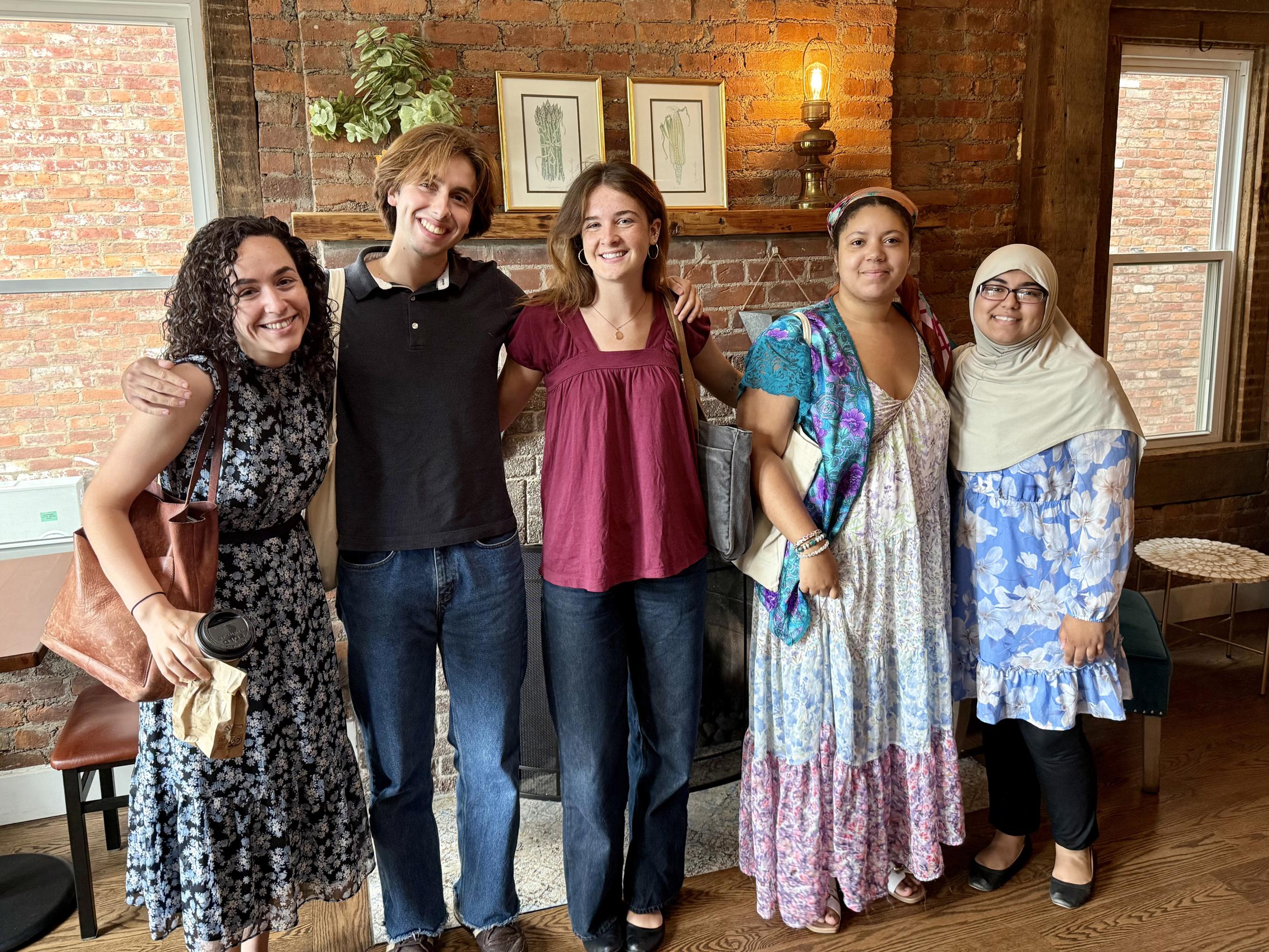 A professor and four students, all smiling, pose in front of a brick fireplace.