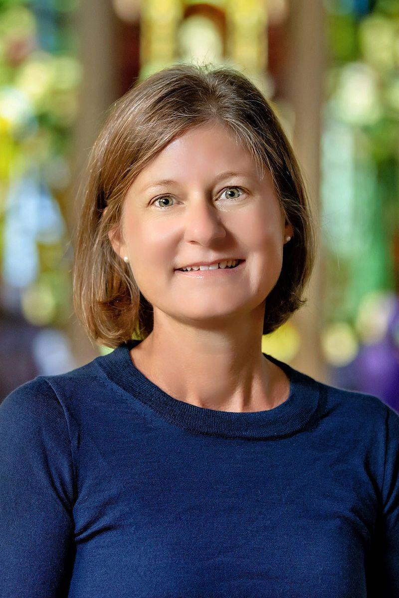 A person smiling with a colorful stained glass window in the background.