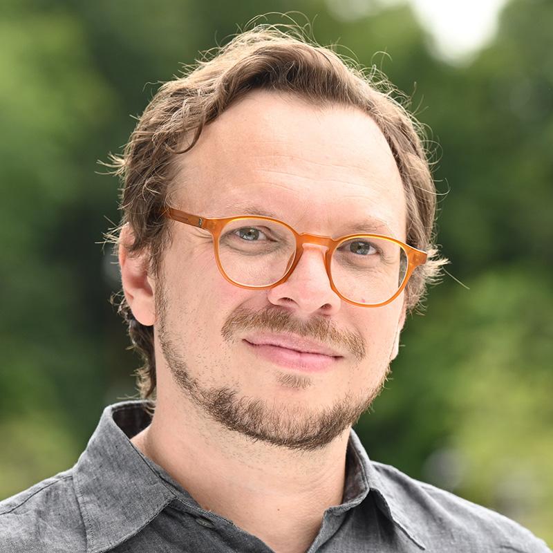 Portrait of a person outdoors wearing orange glasses and a gray shirt.