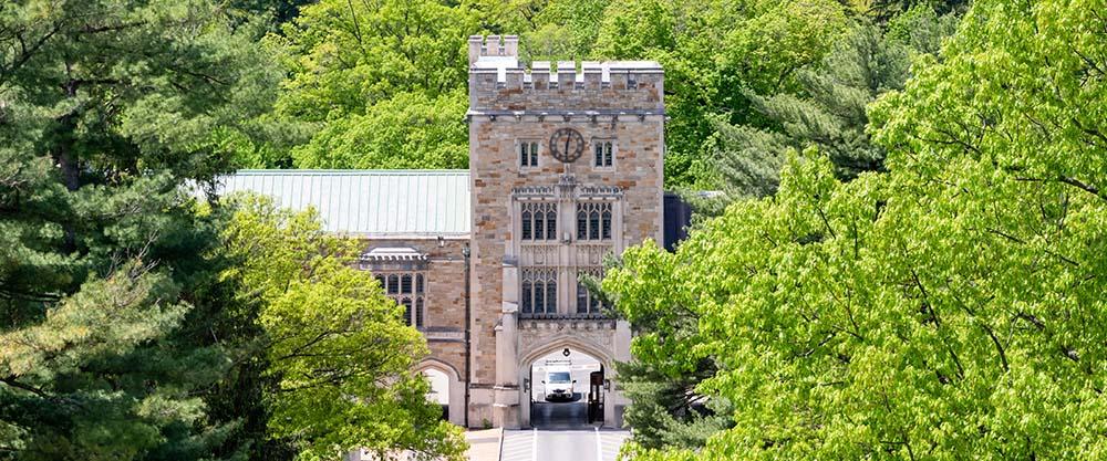 An aerial view of a gothic-style tower gate connected to buildings on either side, with lots of green trees in front and behind it.