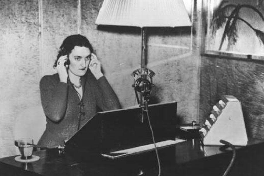 A person sitting at a desk listening intently with her hands pressed to the headphones that cover her ears.