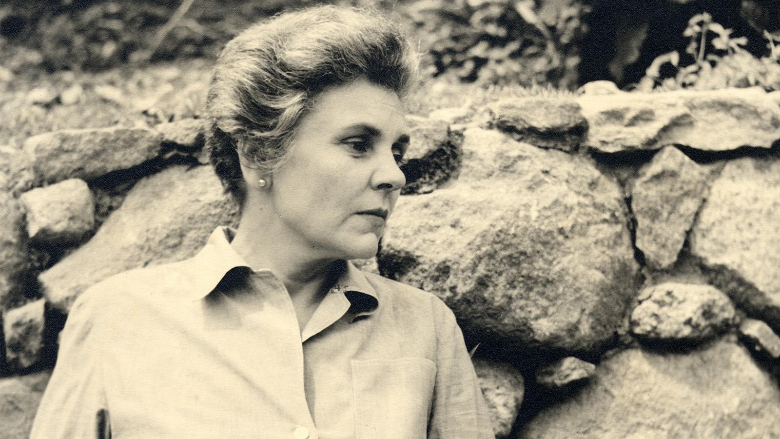 A person in profile leaning against a wall of rock.