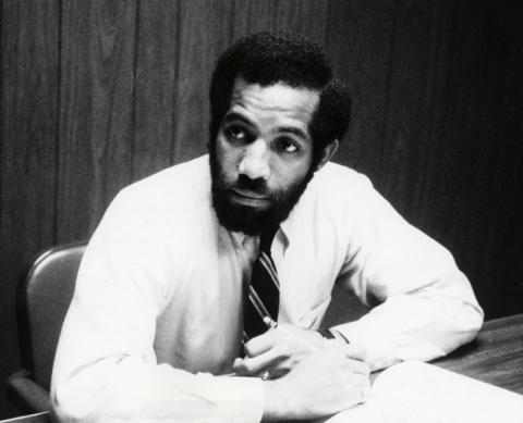 A photo of a person wearing a white shirt and tie, sitting in a chair and looking to their right