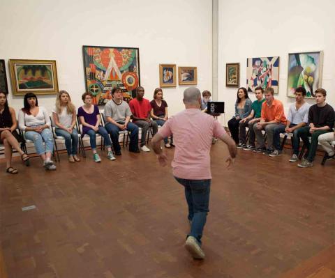 A man dances in an art gallery with the audience seated against the walls.