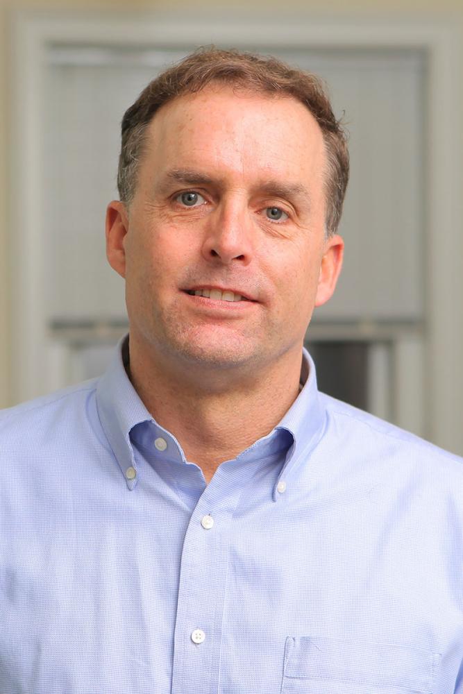 Christopher Bjork with short brown hair and blue eyes, wearing a light blue button-down shirt.