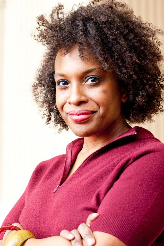 A headshot of Jasmine K. Syedullah, a person with long black curly hair and a dark pink shirt.