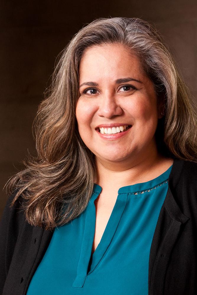 Jennifer Herrera smiling with long brown hair, wearing a teal top and black cardigan.