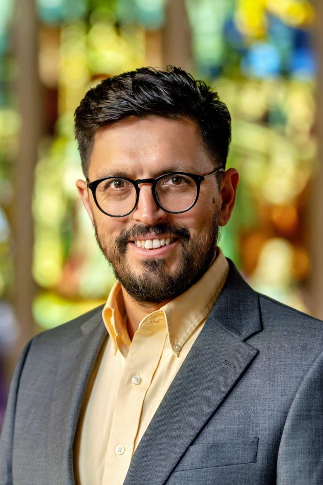 A person smiling with a colorful stained glass window in the background.
