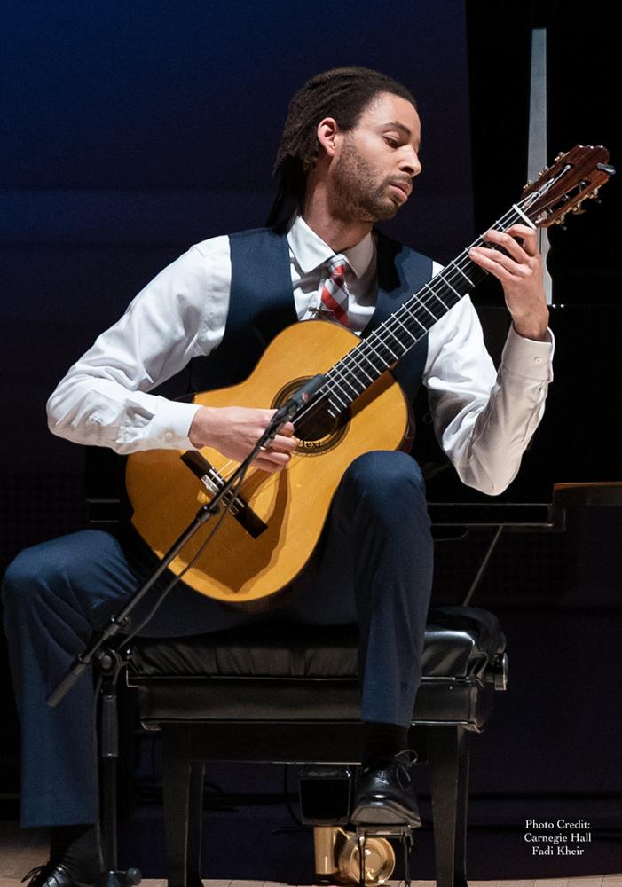 A performer playing the guitar on stage, seated.